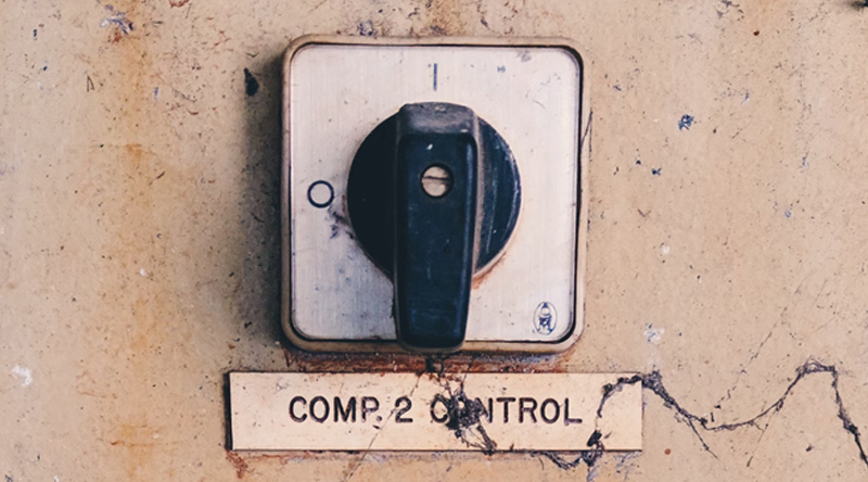 A dial/switch on a control panel. Beneath the switch is a small weathered placard reading COMP. 2 CONTROL.