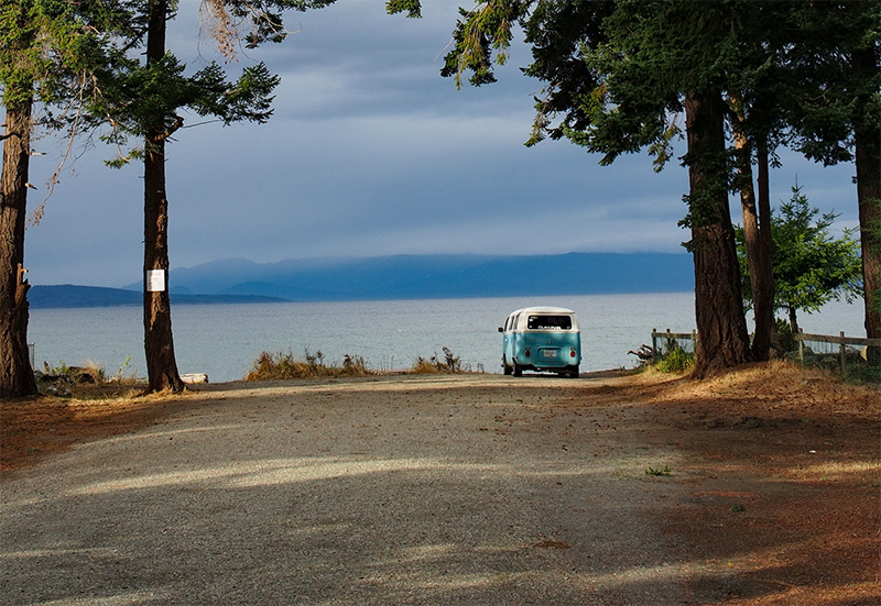 A VW bus at the end of a road leading to a lake