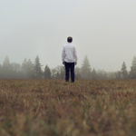 Person standing alone in a foggy field.