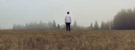 Person standing alone in a foggy field.