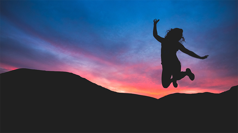 A woman jumping in front of a sunset.