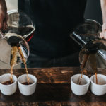 Pouring four cups of coffee from 2 decanters.