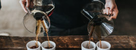 Pouring four cups of coffee from 2 decanters.