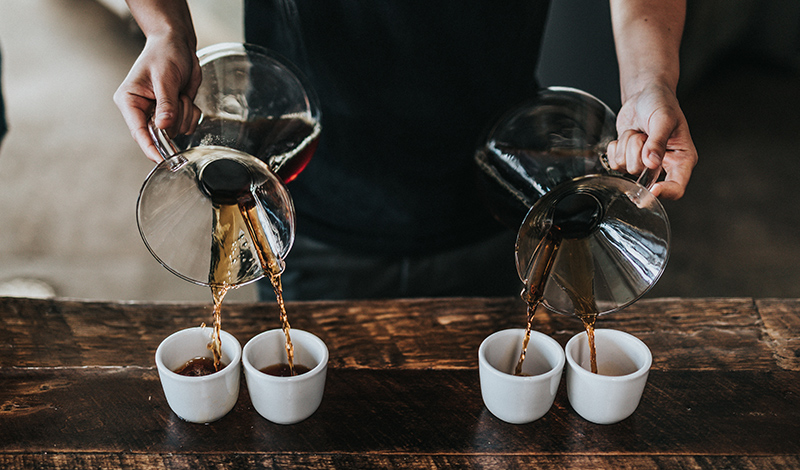 Pouring four cups of coffee from 2 decanters.