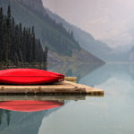 Red canoes on a pier on a still lake.
