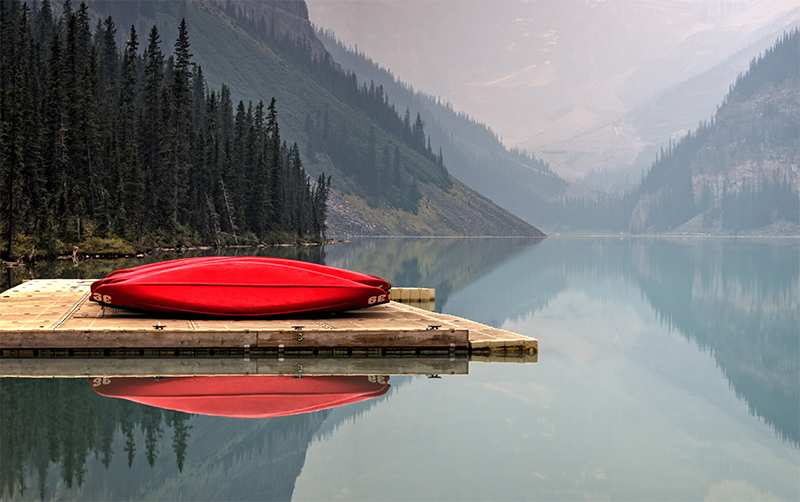 Red canoes on a pier on a still lake.