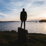 Guy standing on a rock while looking out over water.