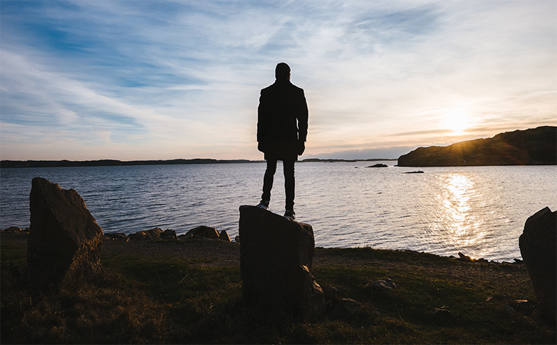 Guy standing on a rock while looking out over water.